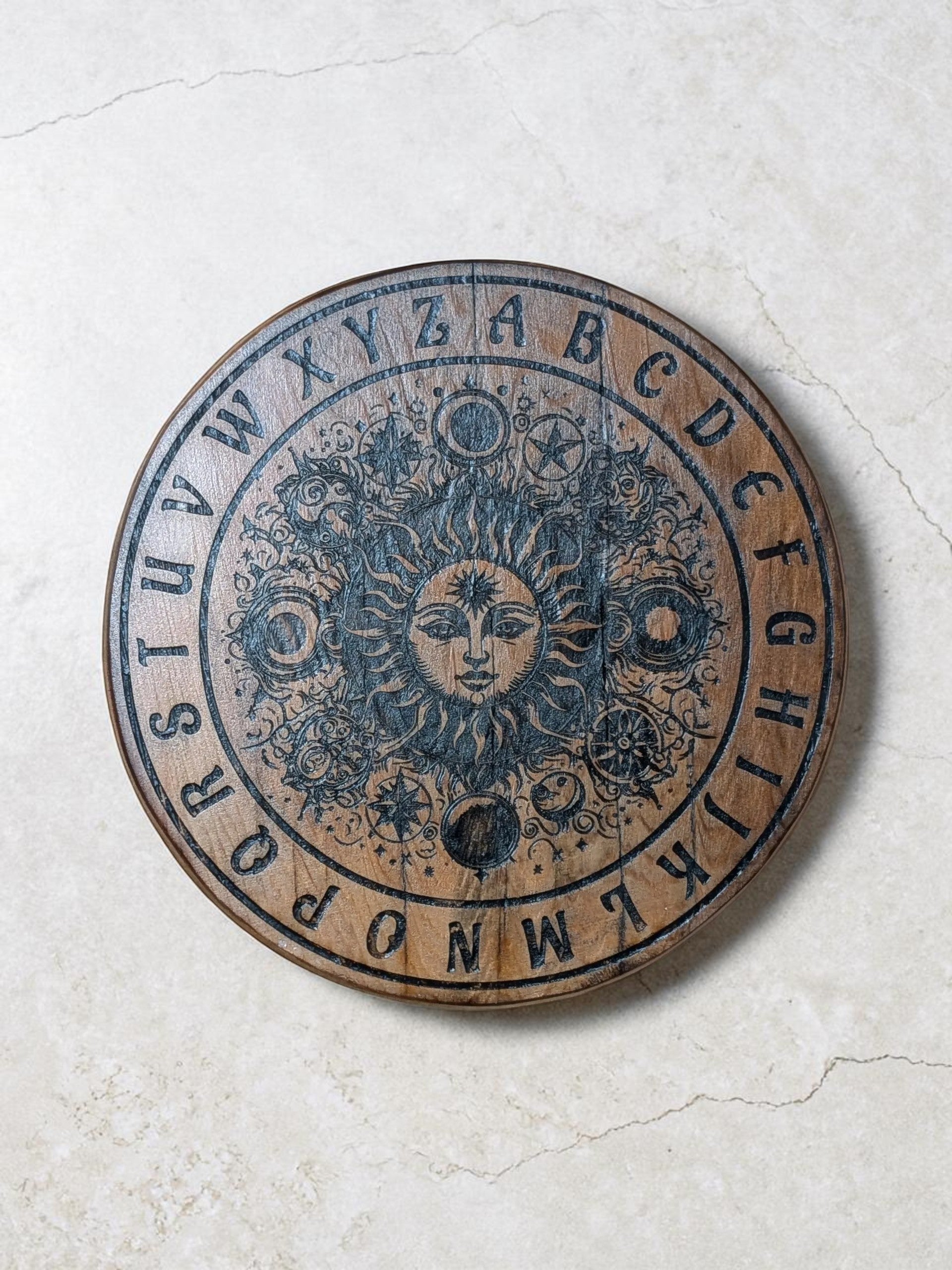 Dogman's Designs wooden pendulum board with sun, moon, and stars design, featuring the alphabet.